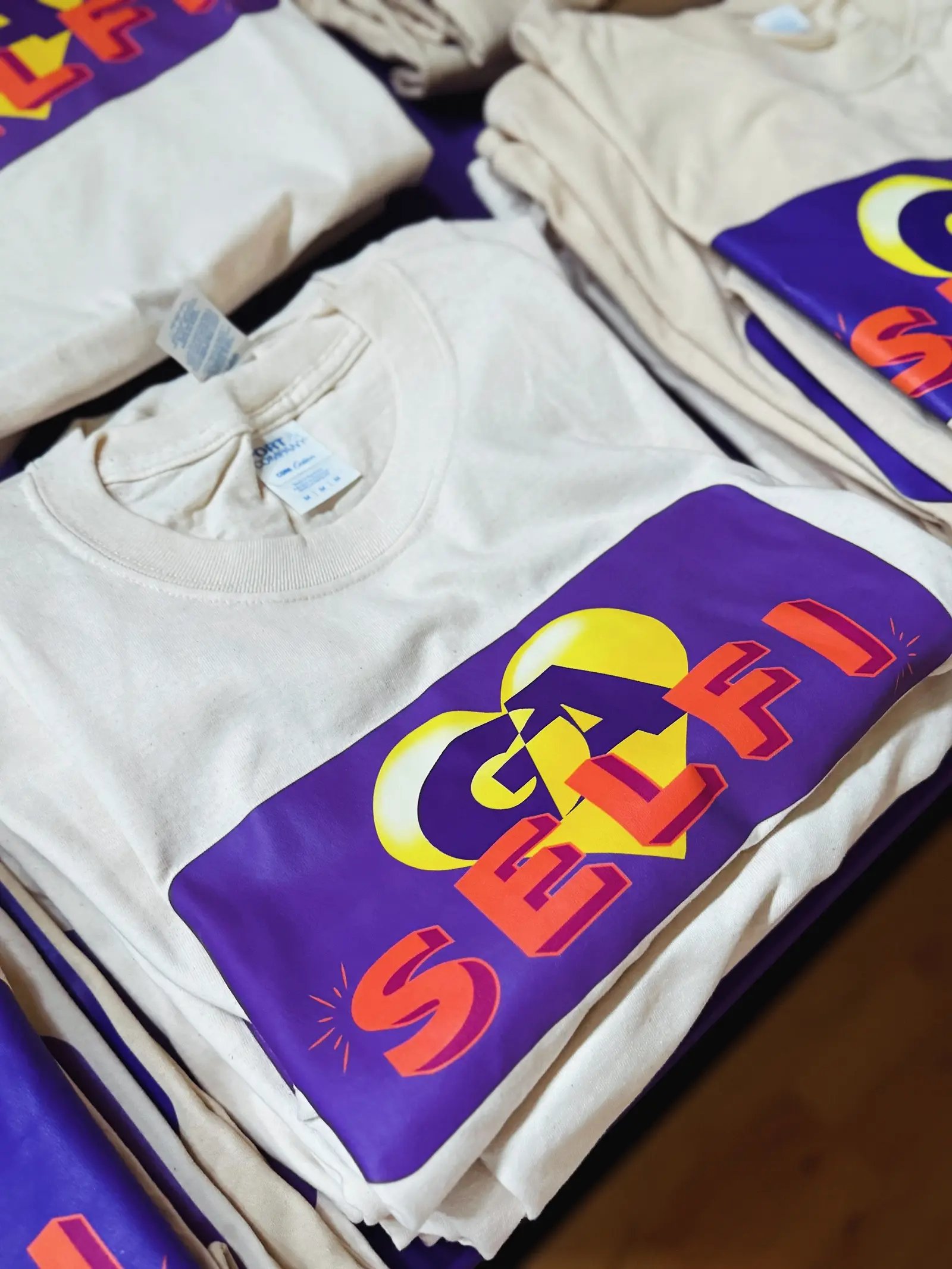 Folded T-shirts stacked on a table beside a purple cloth.