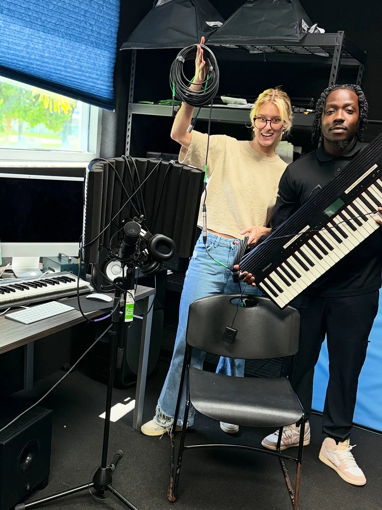 A person standing behind a keyboard in a studio, one arm raised.