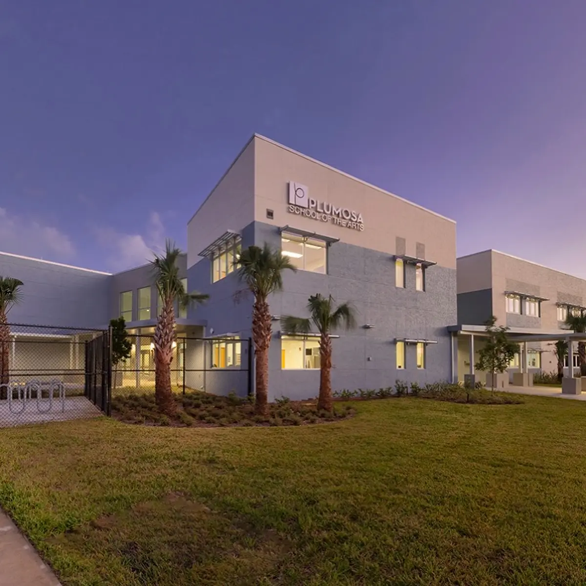 A low school building with palm trees and a lawn in front of it.