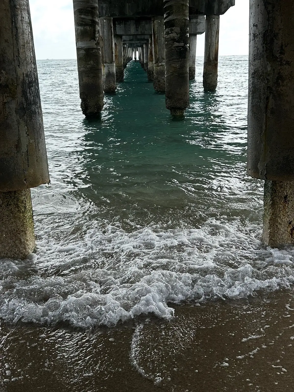 Water moving between the pilings of a pier, photographed from the sand.