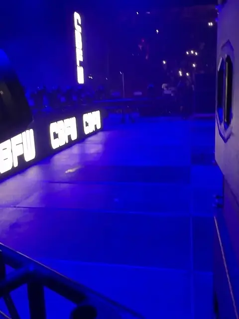 An empty blue-lit venue floor with a large screen at the far end.