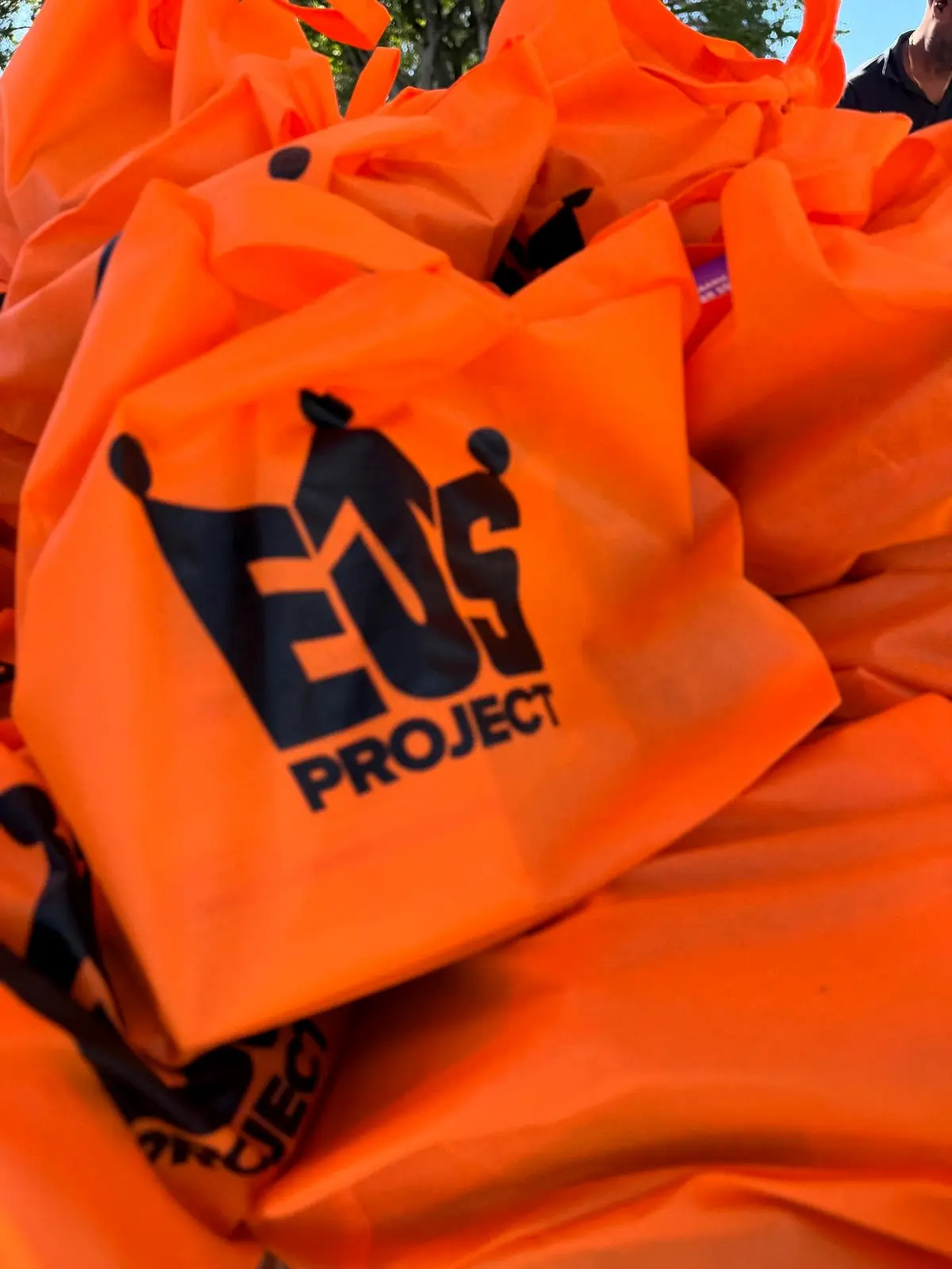 A pile of orange drawstring bags printed with a project logo.