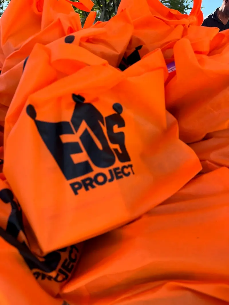 A pile of orange drawstring bags printed with the organisation's mark, stacked before a distribution.