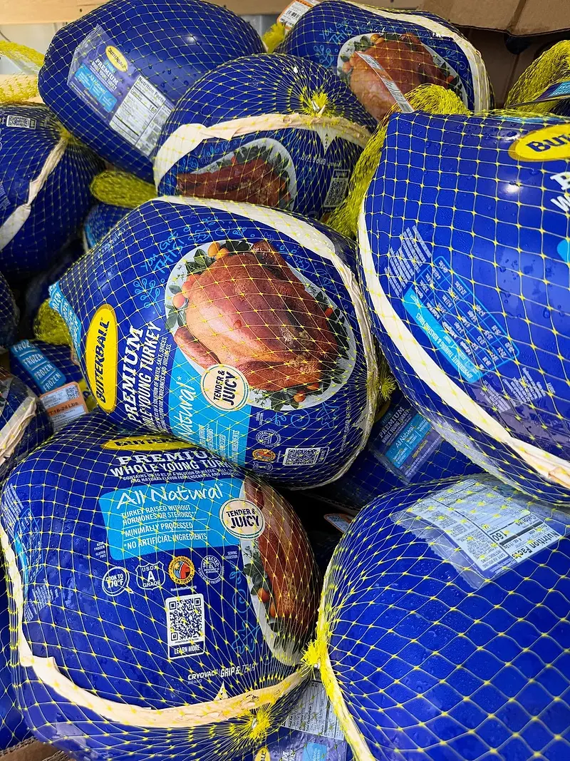 A stack of frozen whole turkeys in blue and white netting and branded plastic wrapping.