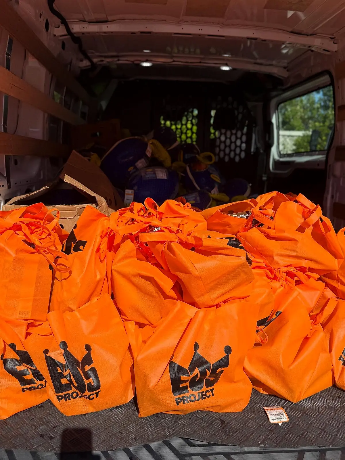 A van loaded with orange drawstring bags printed with a project logo.