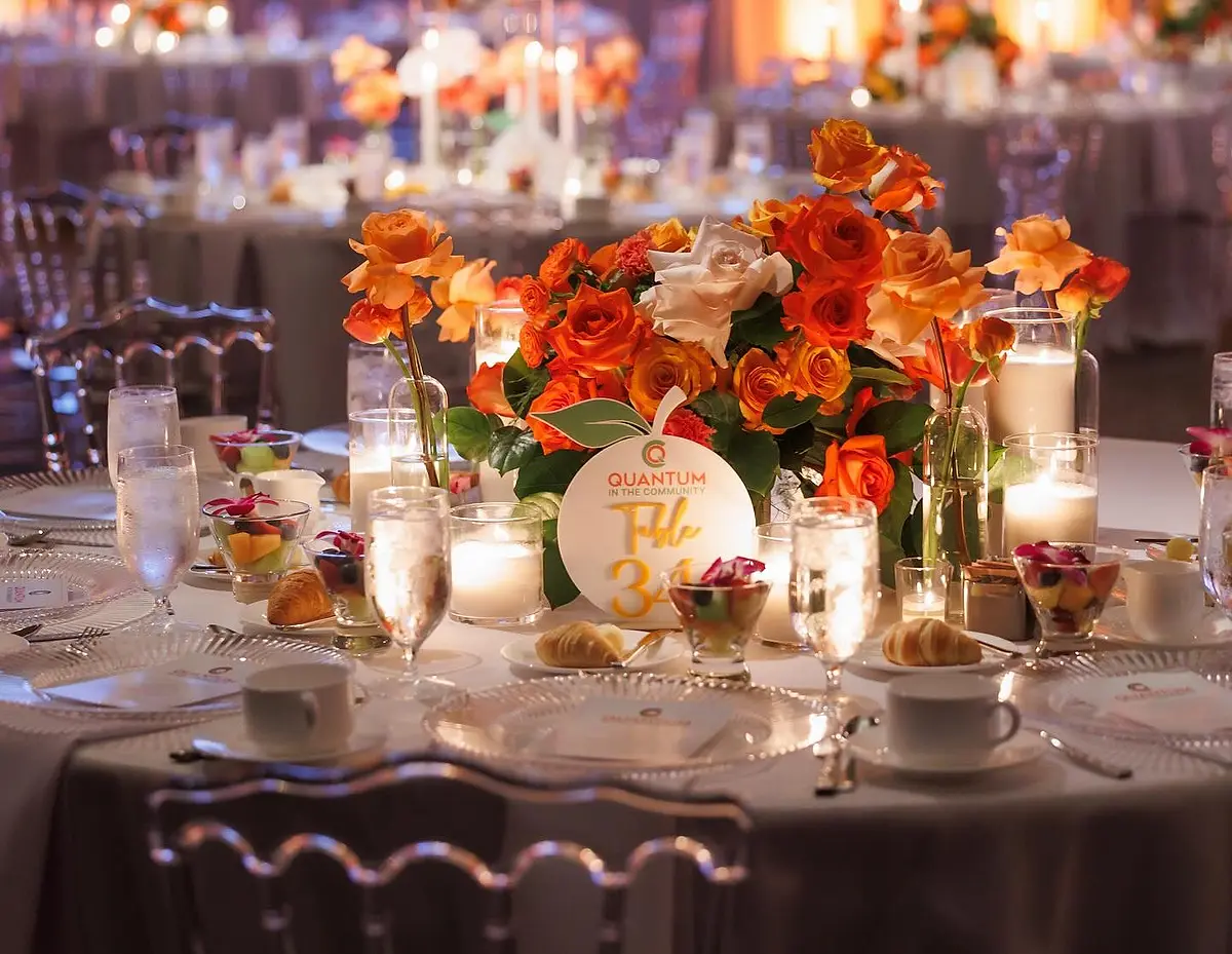 A round banquet table set with glassware, candles and an orange and rose centerpiece.