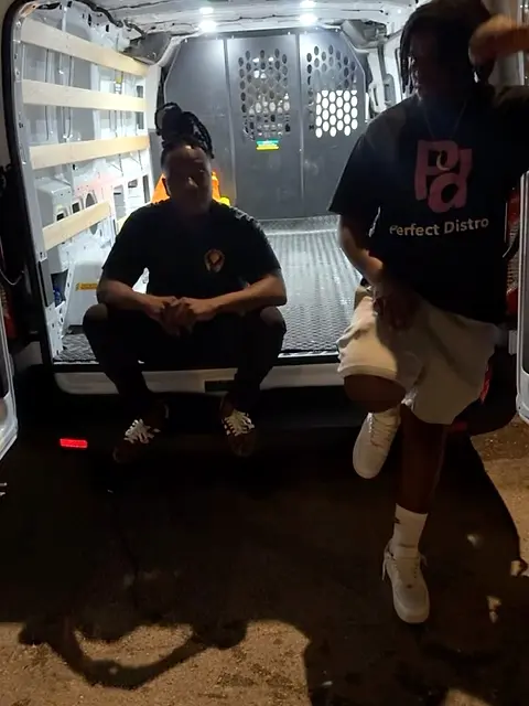 Two people carrying bags at the open side door of a van.