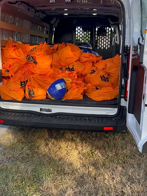 The open rear doors of a van filled to the roof with orange drawstring bags.