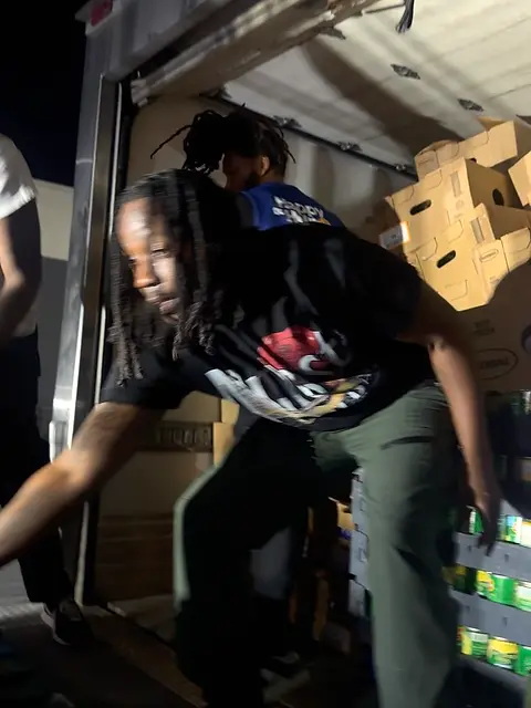 A person lifting a box of food at the open door of a van.