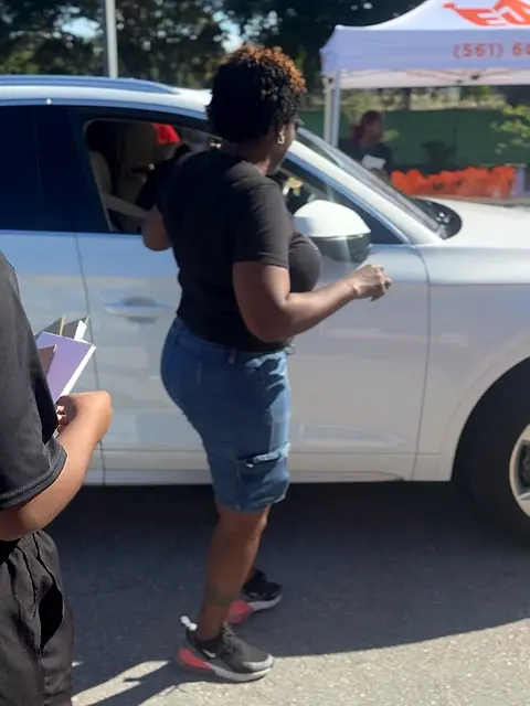 Someone reaching into the open boot of a car to hand over a bag.