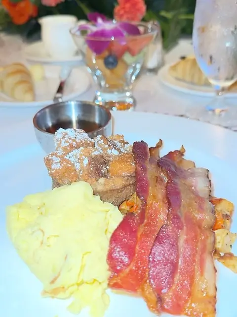 A plate of pancakes, eggs and bacon served on a paper plate.